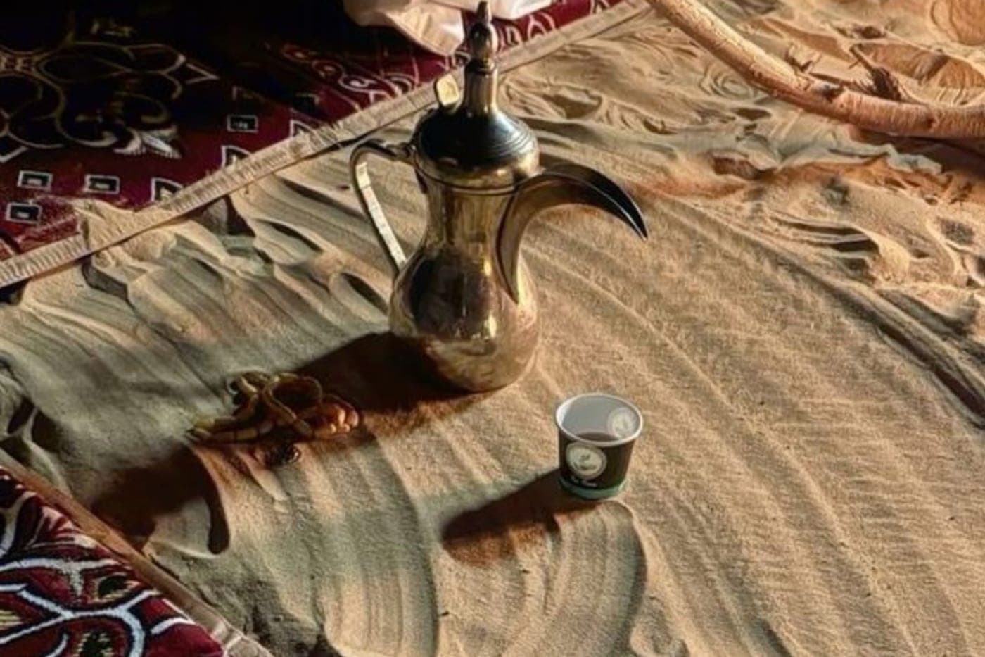 A brass dallah and a cup of Saudi coffee on the sand at a desert majlis
